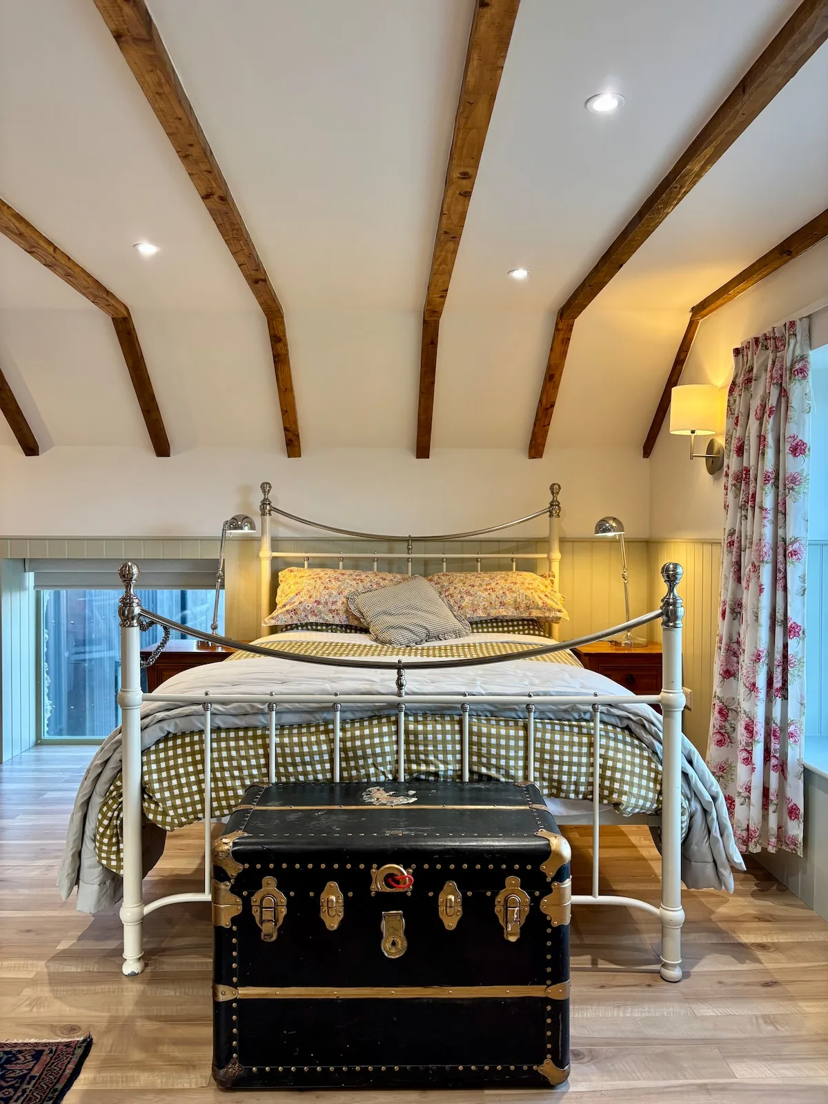 Iron-framed bed with vintage trunk under exposed beams